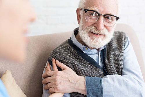 Elderly man in glasses smiling up at a doctor with her hand on his shoulder